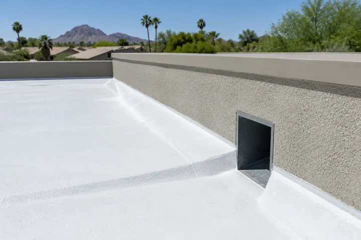 Roof scupper through a parapet wall on a white-coated foam flat roof, sloped foam leading water to it