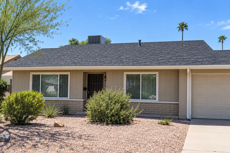 The same single-story Tempe ranch house from the same front angle after reroofing: new charcoal architectural shingles, fresh painted fascia, straight new gutter, sunny day
