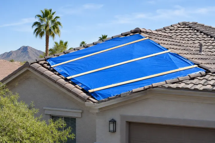 Blue protective tarp neatly secured with wood strips over a damaged section of a residential roof