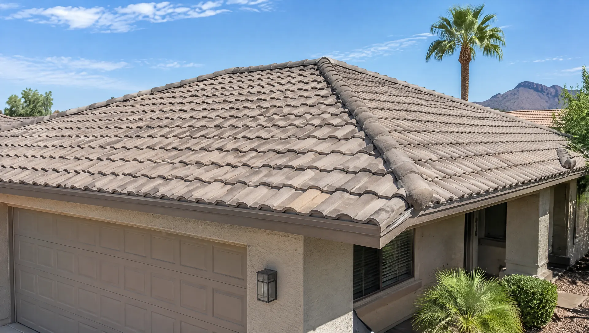 Low-slope concrete S-tile roof on an Arizona ranch home after repair: a few new replacement tiles blended in, straight courses, mortared ridge line, palm tree in the background, bright sky