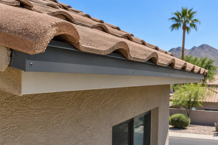 New metal drip edge and eave closure strip at the bottom edge of a tile roof, with the first row of tiles set above it